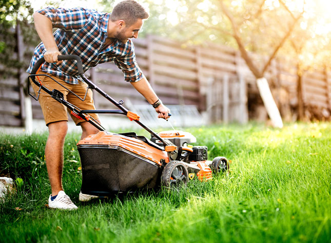 Man mowing yard with an orange push mower.